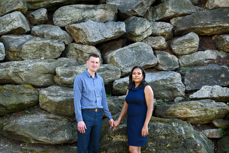 A bride and groom to be stand in front of a rock wall near the Schuylkill River.